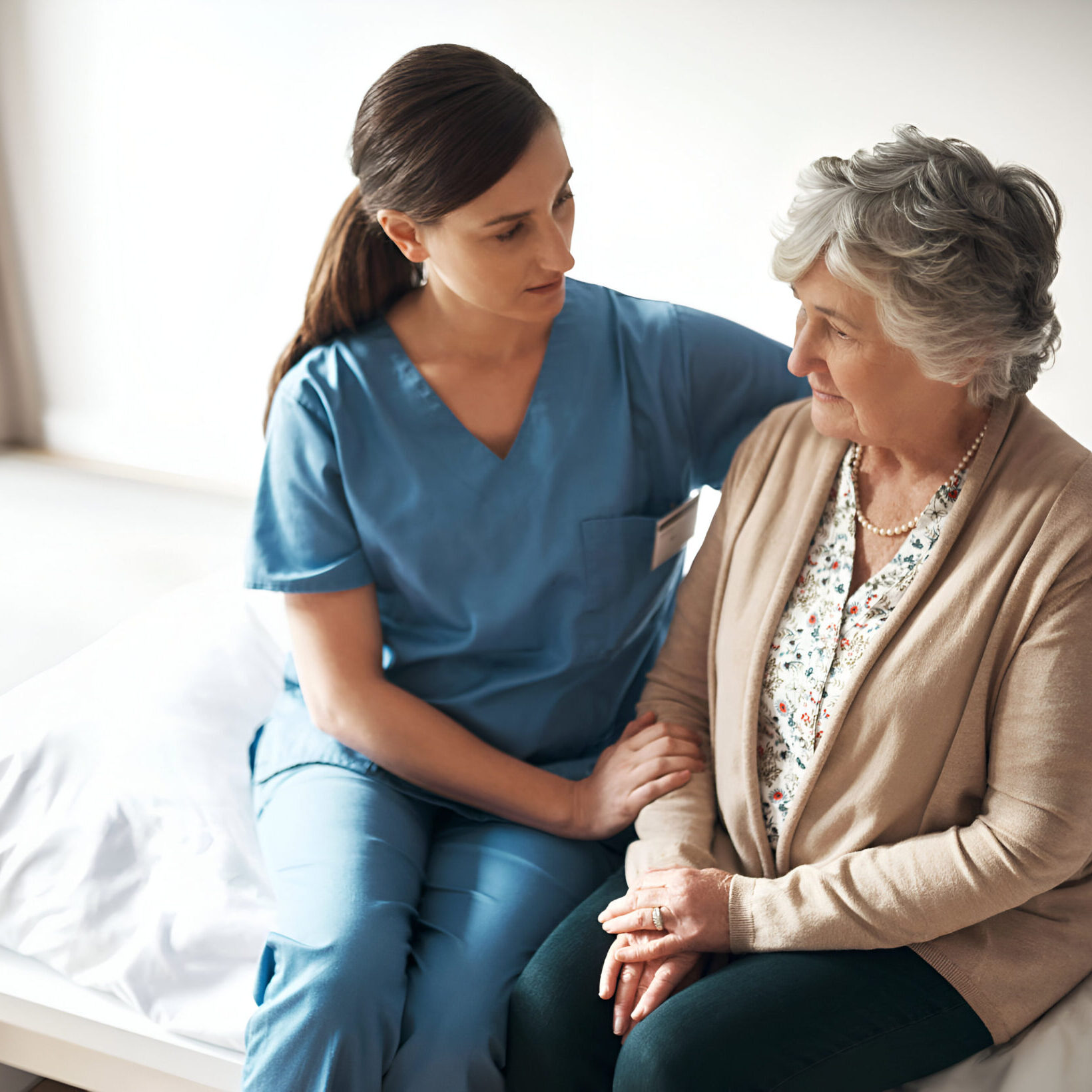 A senior woman and nurse speaking in the bedroom on a bed.